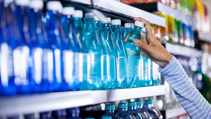 Woman picking bottle of water in grocery section of supermarket.