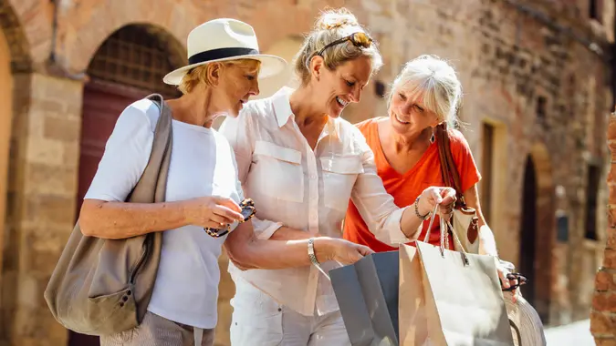 A woman stands in an old part of town in Italy holding shopping bags.