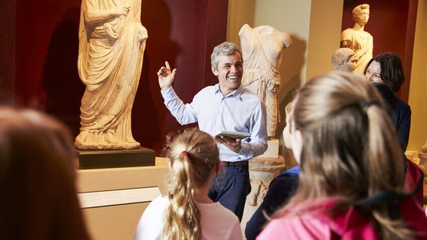Pupils And Teacher On School Field Trip To Museum With Guide.