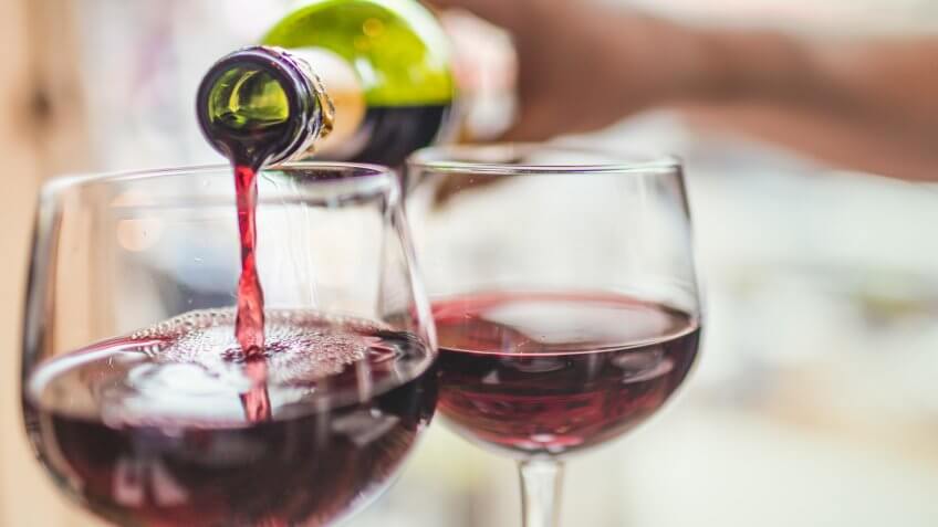 Unrecognizable man pouring red wine in two glasses.