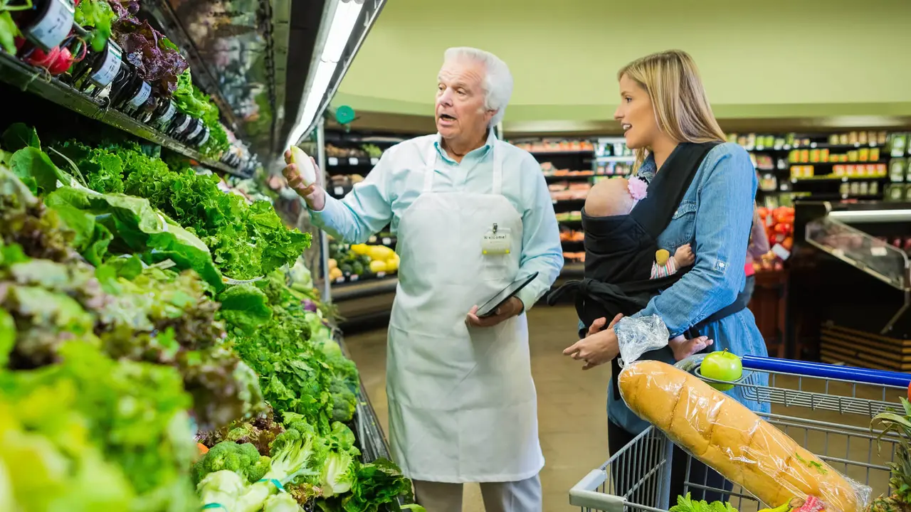 Senior grocery store employee assisting customer in produce section