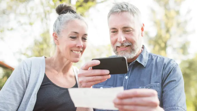 A gray haired and youthful looking couple in their 50's enjoy time with each other in a beautiful outdoor setting, the sun casting a golden glow on the scene.