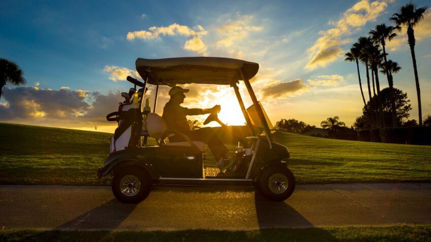 Senior man on golf course driving golf cart at sunrise.