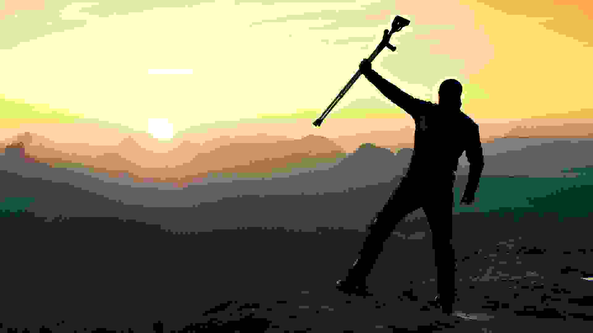 Tourist with forearm crutch above head achieved mountain peak.