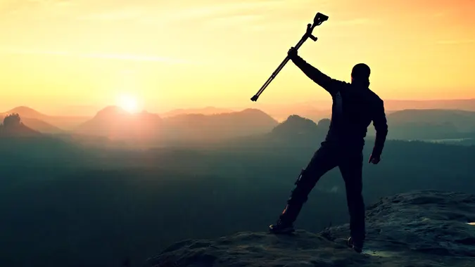 Tourist with forearm crutch above head achieved mountain peak.