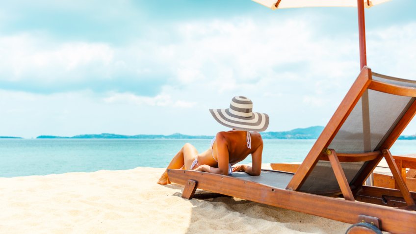 Woman in sunhat sunbathing in beach chair.