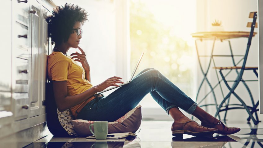 Full length shot of an attractive young woman using her laptop while chilling at home.