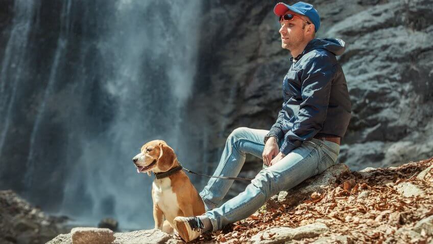 Man with dog sitting near waterfall.