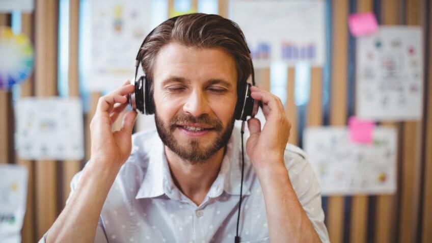 Close-up of male graphic designer listening music on headphone in office.