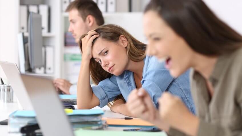 Worried worker beside a successful one who is excited reading good news on line at office.