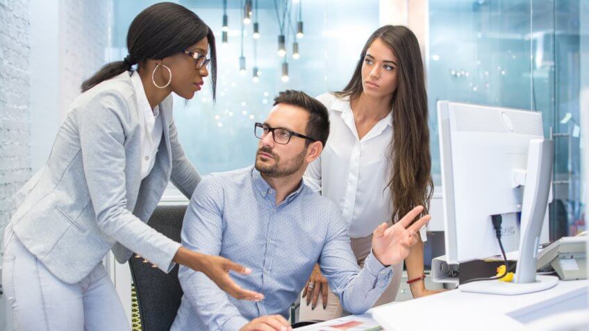 Group of three business people discussing some document on desktop computer in modern office.