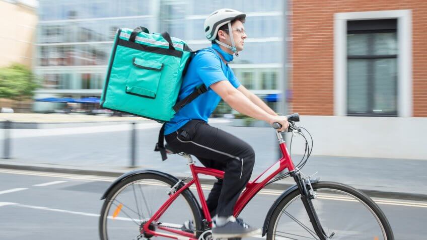 Courier On Bicycle Delivering Food In City.