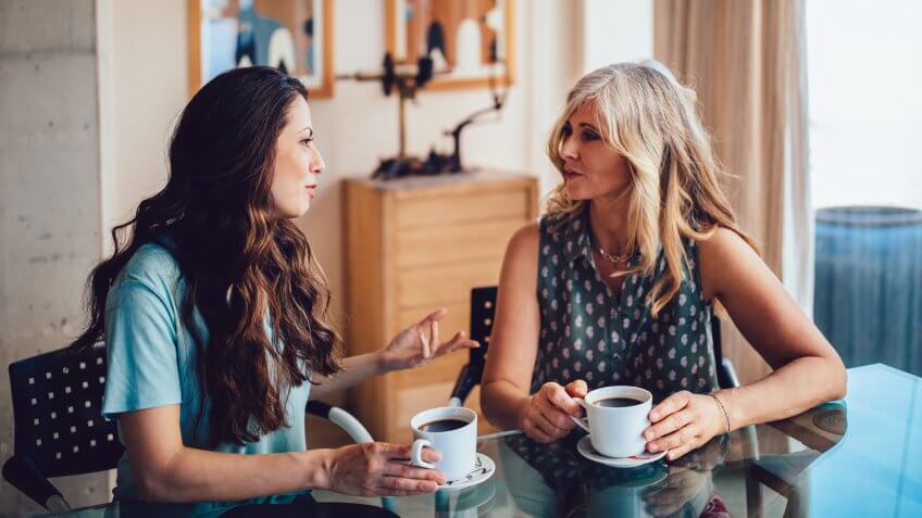 Older mother and daughter spending time together at home drinking coffee and discussing.