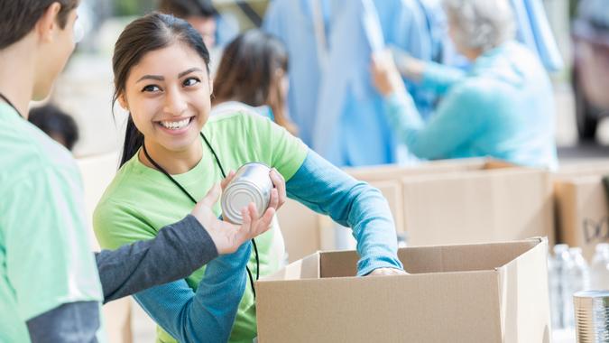 Male and female teenage food bank volunteers sort canned food items in cardboard boxes.