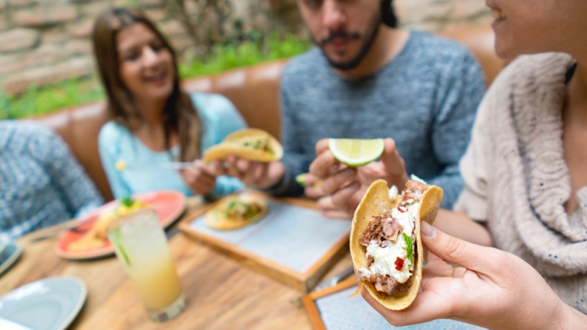 Group of friends eating tacos at a Mexican restaurant looking very happy.