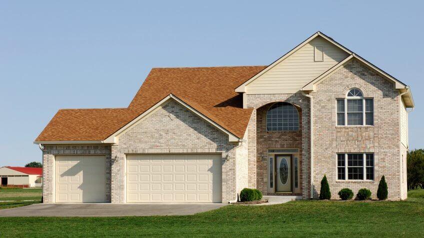 Two story light colored brick home with 3 car garage in suburbia.