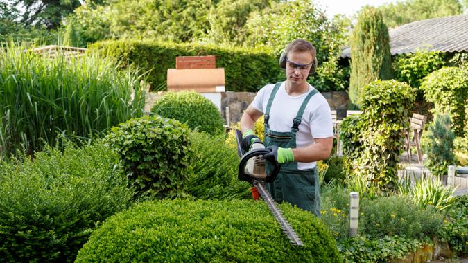 man using hedge trimmer on home landscape
