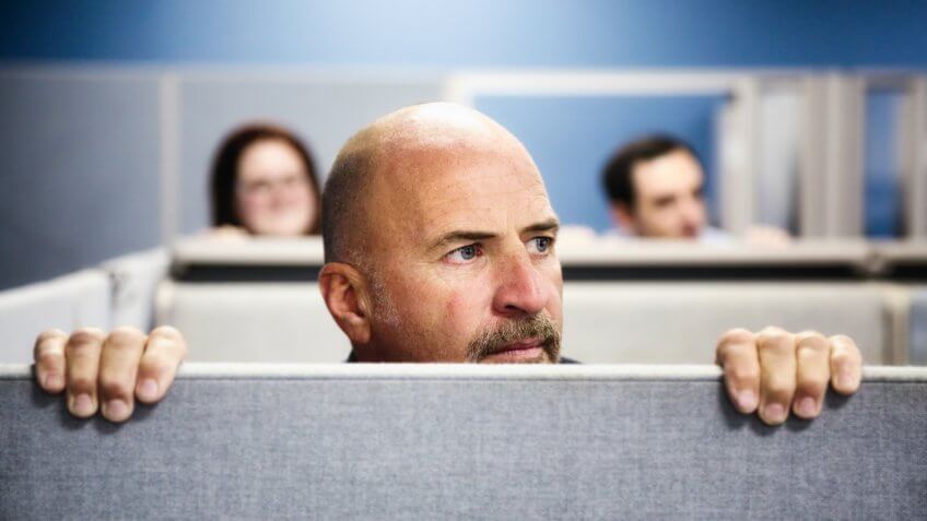 Three office worker look over their cubicle to the right with concern.