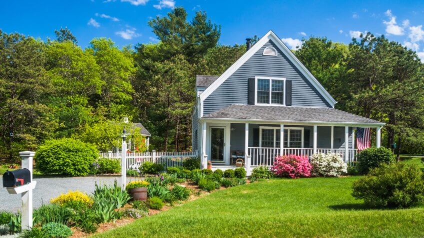 An American flag flies from the open porch and gardens surround a small single family home on a Spring afternoon on Cape Cod on the Massachusetts coast.