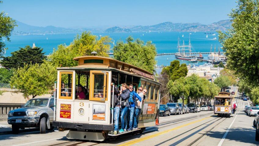 People ride cable car in San Francisco, California, USA on a sunny day.