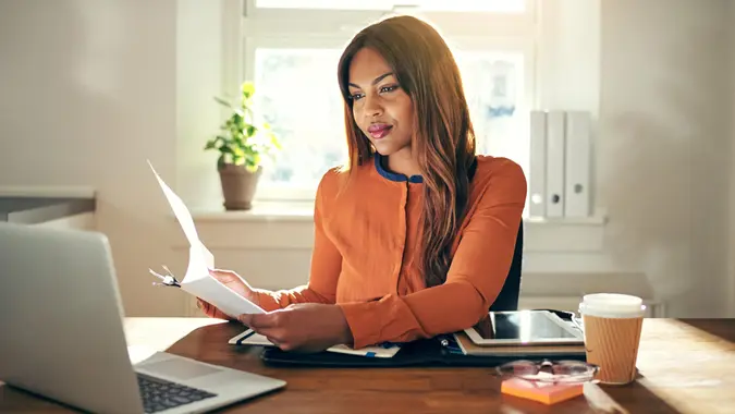 Woman in orange cardigan at desk at home looking at laptop