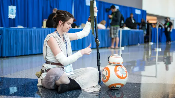 A cosplayer dressed up as Rey from Star Wars gives the thumbs up to a BB-8 drone