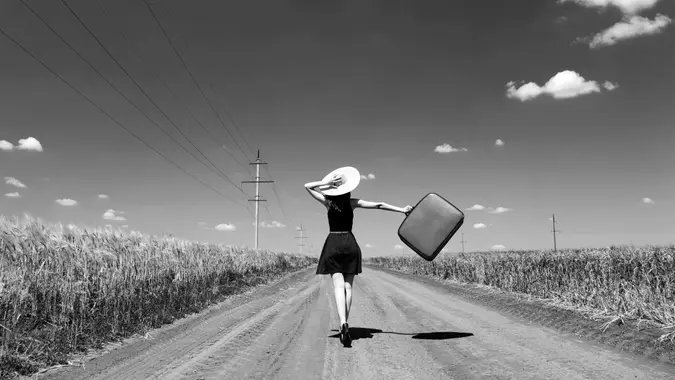 Lonely girl with suitcase at country road.