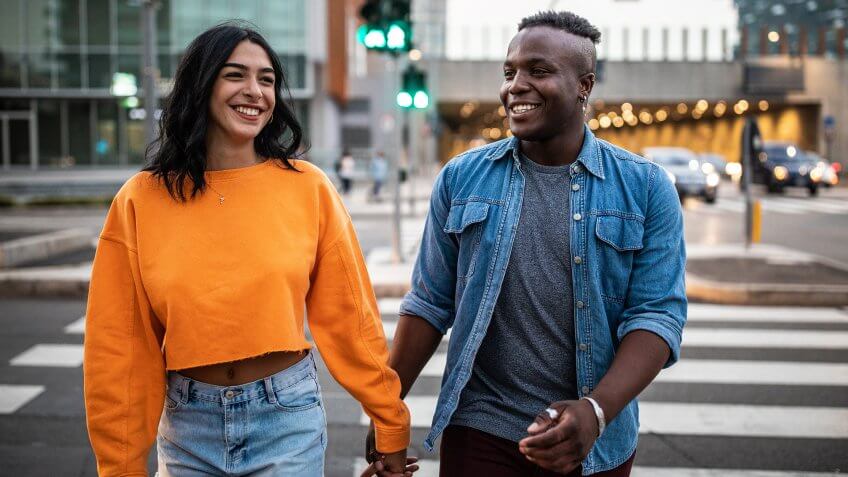Beautiful cheerful couple crossing street on zebra crossing, holding hands and smiling.