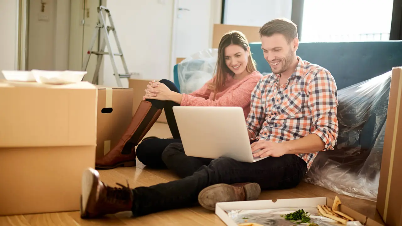 Young couple surrounded by moving boxes, symbolizing relocating, buying a first home, or preparing to move into a new apartment or recently purchased property.