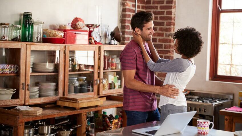 Young mixed race couple embracing in kitchen, waist up.