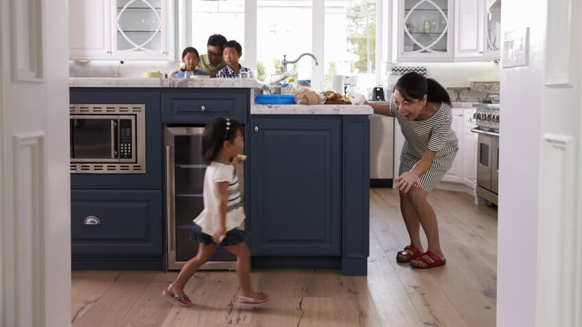 Parents Prepare Food As Children Play In Kitchen.