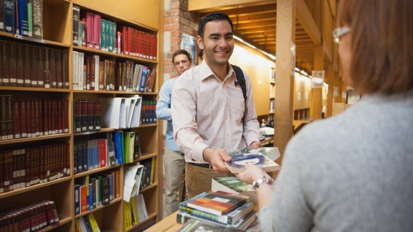 Mature female librarian handing a book to young man in library.