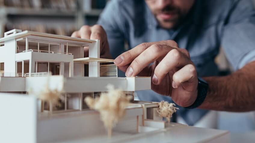 Close up of male architect hands making model house.