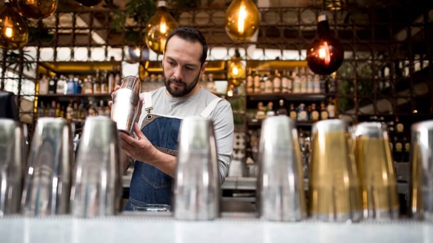 Latin American bartender mixing drinks at a bar in a cocktail mixer.