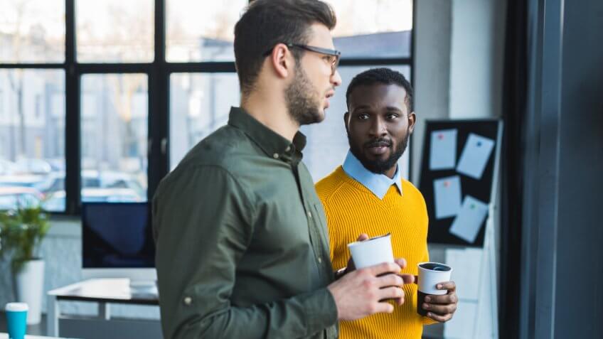 multicultural businessmen talking and holding cups of coffee.