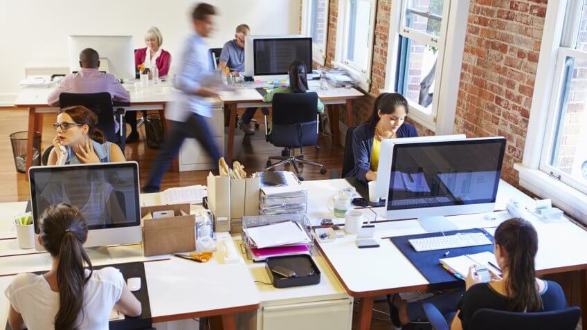 Wide Angle View Of Busy Design Office With Workers At Desks.