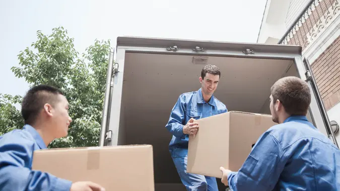 Movers unloading a moving van, passing a cardboard box.