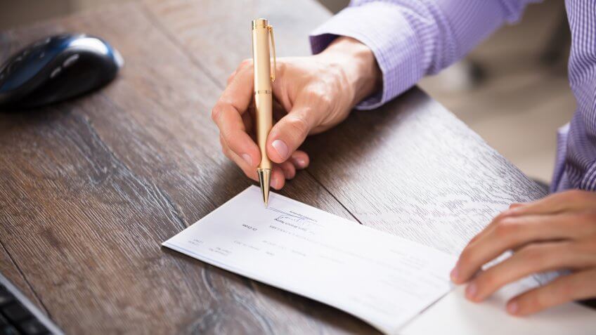 Close-up Of A Businessperson's Hand Signing Cheque In Office.