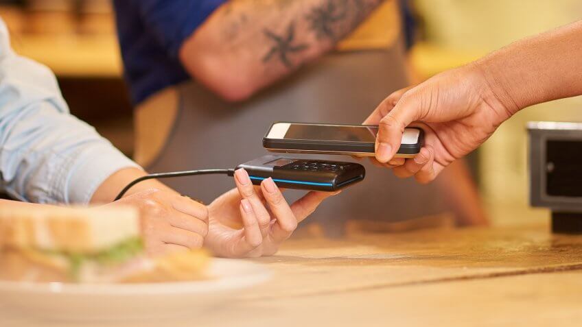 A female barista holds the card machine for her customer to pay.