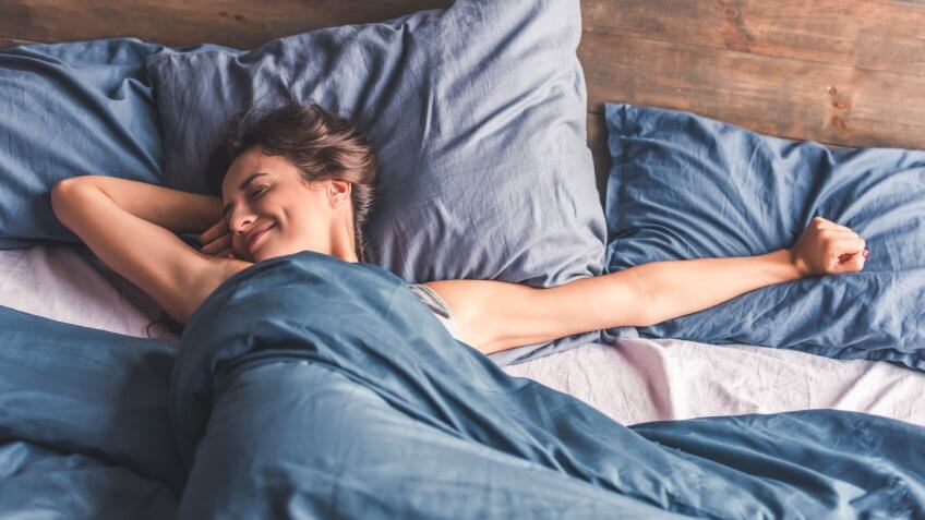 Beautiful young woman is stretching and smiling while lying in bed in the morning.