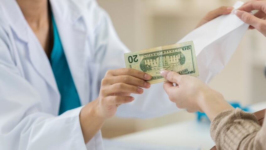 Unrecognizable female pharmacy customer hands pharmacy employee a twenty dollar bill to pay for prescription medication.