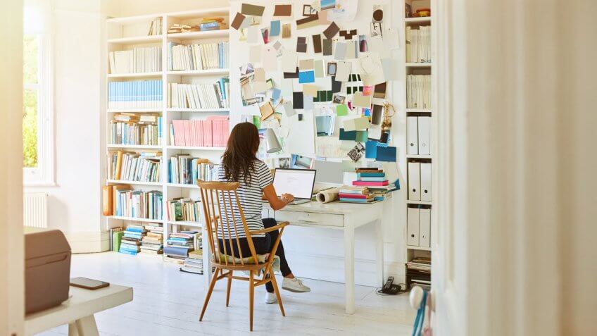Rear view of pregnant woman sitting in home office and working on laptop.
