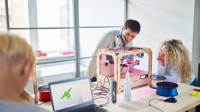 Group of young engineers making prototype of plane with 3D printing in technology laboratory and observing process.
