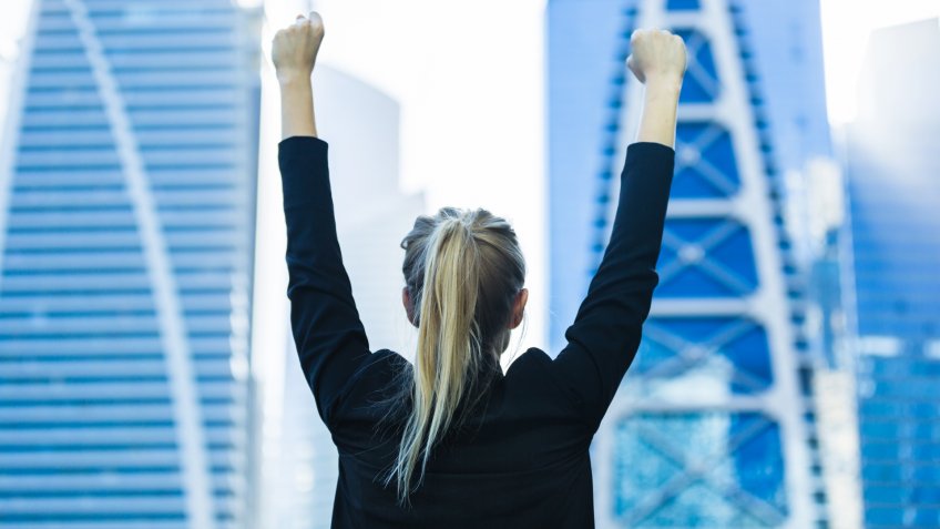 Business success - Celebrating businesswoman overlooking the city center high-rises.