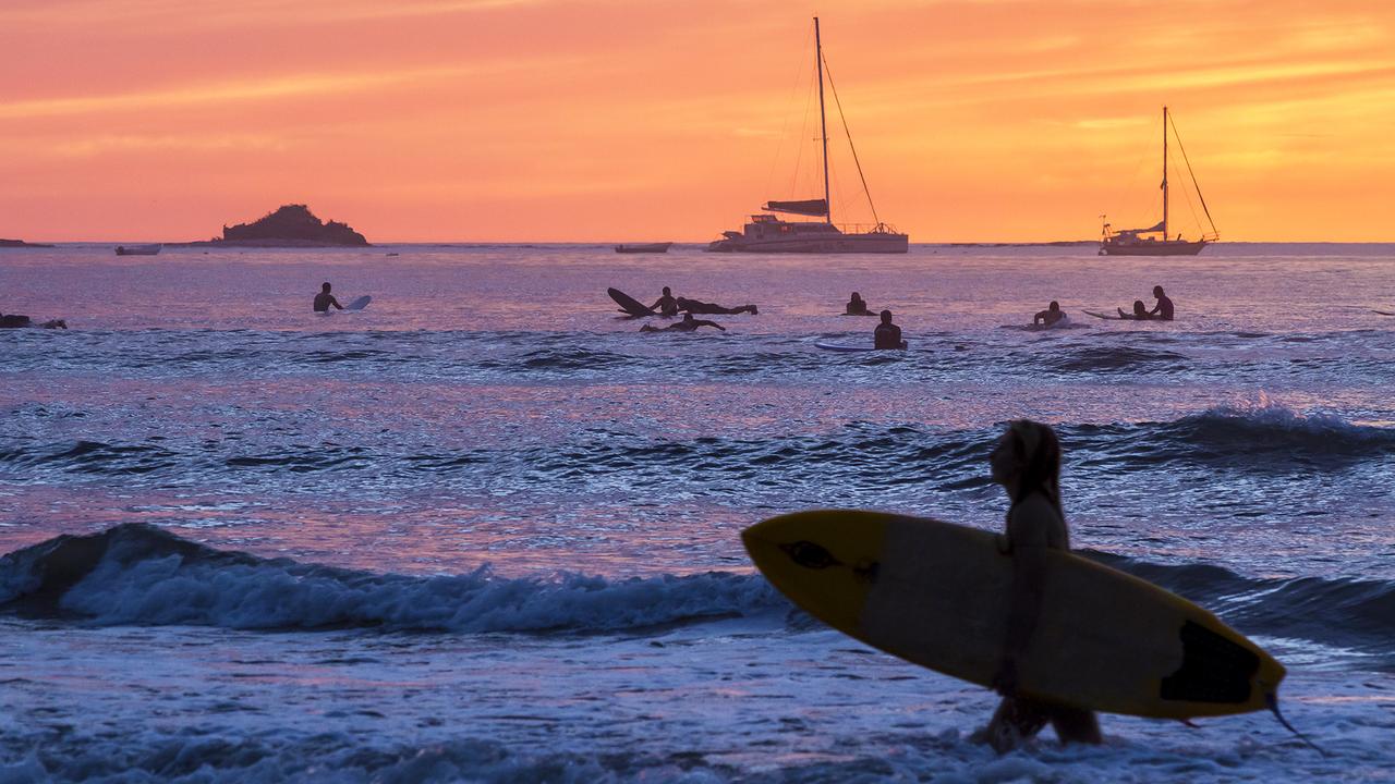 Surfers silhouetted against a brillinatly colored sunset on Playa Tamarindo, Guanacaste, Costa Rica.