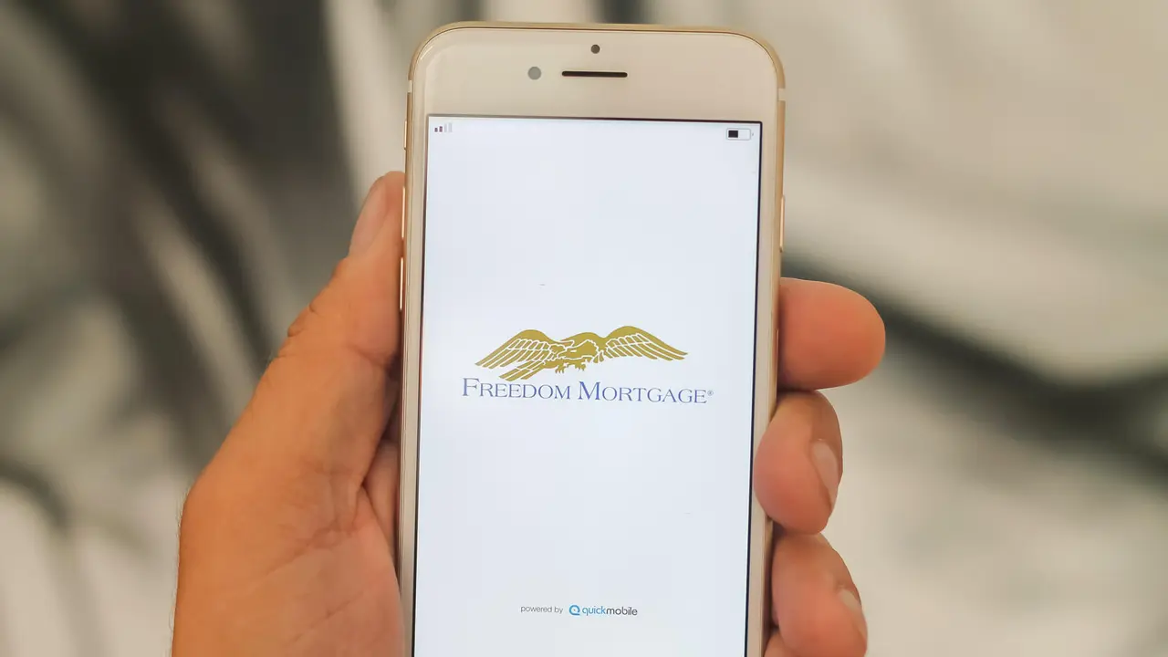 Hand holding a mobile phone that is displaying the freedom mortgage logo on the white, bright screen