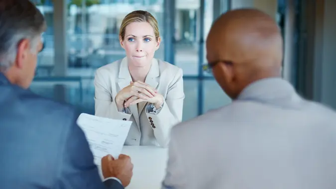 Tensed business woman sitting in front of panel of interviewers.
