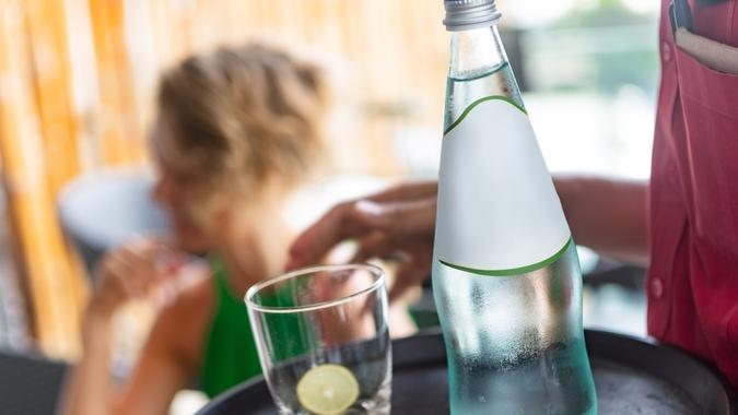 Wait staff serving water, carrying water bottle and drinking glasses on serving tray.