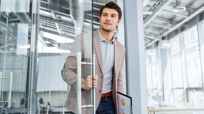 Handsome young businessman with clipboard entering the door in office.