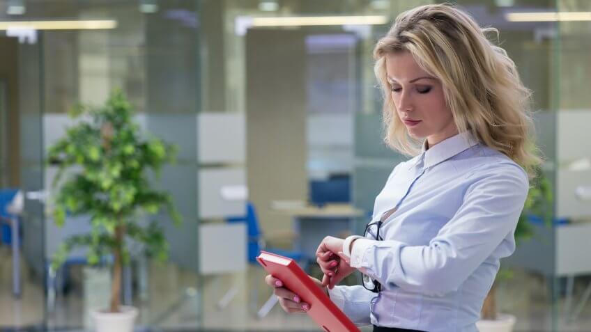 Elegant blonde businesswoman with red notepad in her hand checking time.